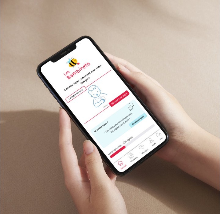 Personne tenant son smartphone. On peut y voir sur l'écran, le prototype d'une application mobile dédié à l'apprentissage du langage des signes.