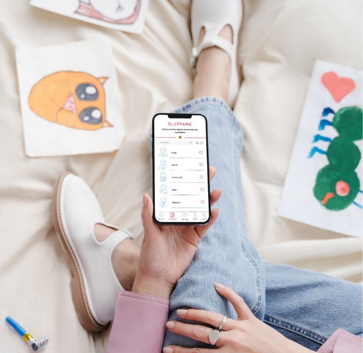 Photo montrant une personne assise sur un lit, consultant une application dédiée à l'apprentissage du langage des signes.