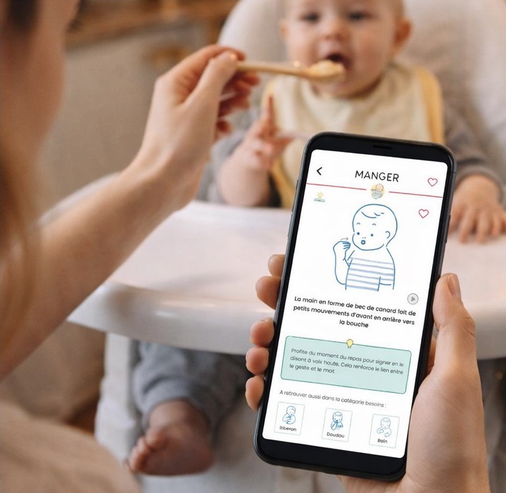Photo montrant une maman qui donne à manger à son bébé. Elle consulte en même temps son smartphone car elle utilise une application pour apprendre le langage des signes bébé.