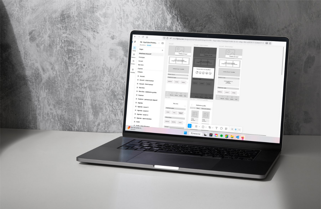 Ordinateur portable ouvert sur une page Figma. Un wireframe est en cours de création on peut voir les différentes pages.